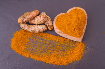 Curcumin powder, arranged into a heart shape, positioned next to raw curcumin root on a purple background
